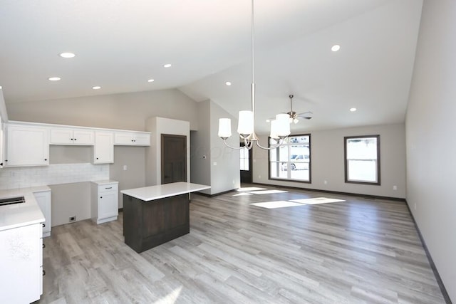 kitchen with backsplash, white cabinets, ceiling fan with notable chandelier, decorative light fixtures, and a kitchen island