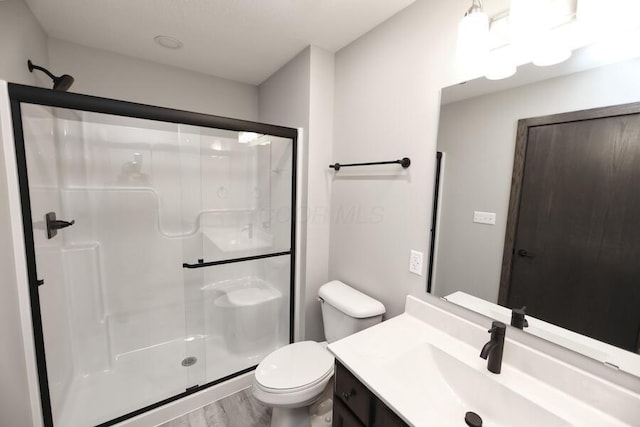 bathroom featuring hardwood / wood-style floors, vanity, a shower with shower door, and toilet