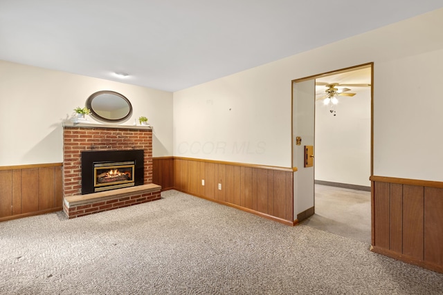 unfurnished living room featuring light carpet, wooden walls, ceiling fan, and a brick fireplace