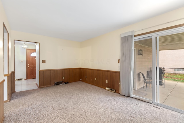 carpeted spare room with a chandelier, a baseboard radiator, and wood walls