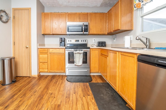 kitchen featuring appliances with stainless steel finishes, a textured ceiling, light hardwood / wood-style flooring, and sink