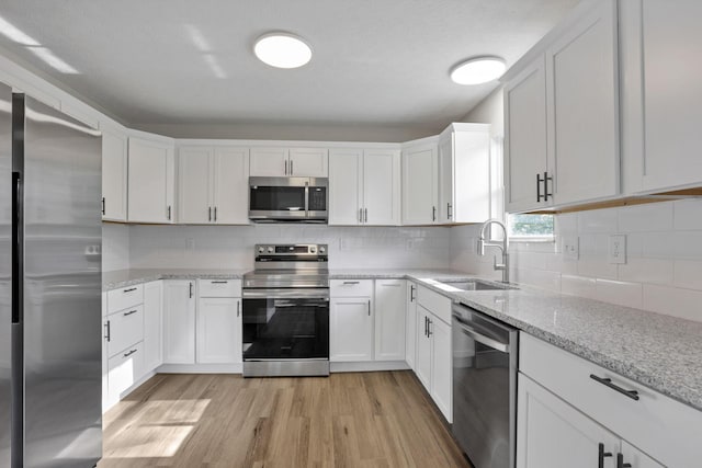 kitchen featuring sink, light wood-type flooring, appliances with stainless steel finishes, light stone counters, and white cabinetry