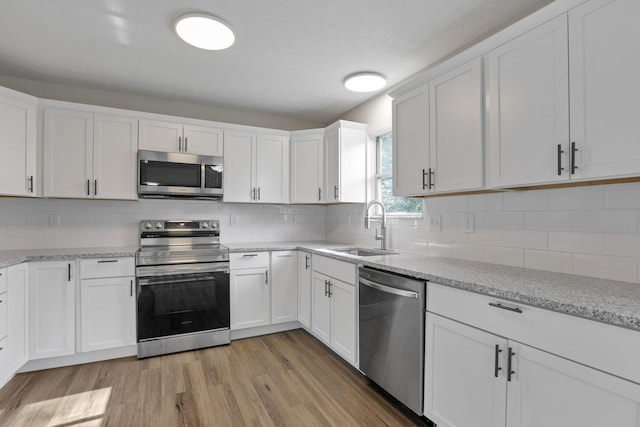 kitchen with tasteful backsplash, stainless steel appliances, sink, white cabinets, and light hardwood / wood-style floors