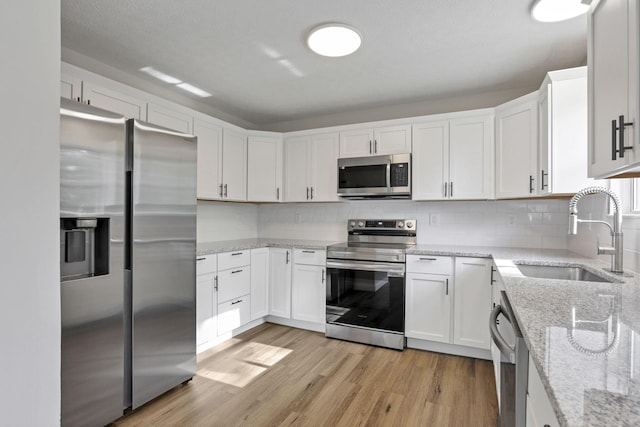 kitchen with white cabinets, sink, light stone countertops, appliances with stainless steel finishes, and light hardwood / wood-style floors