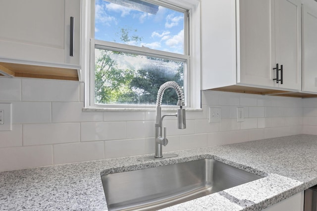 kitchen with decorative backsplash, light stone counters, white cabinetry, and sink