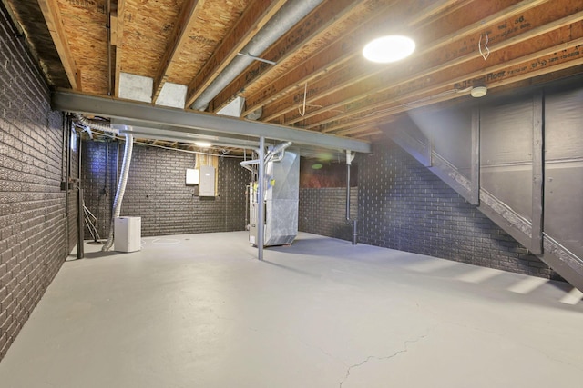 basement featuring electric panel, heating unit, and brick wall