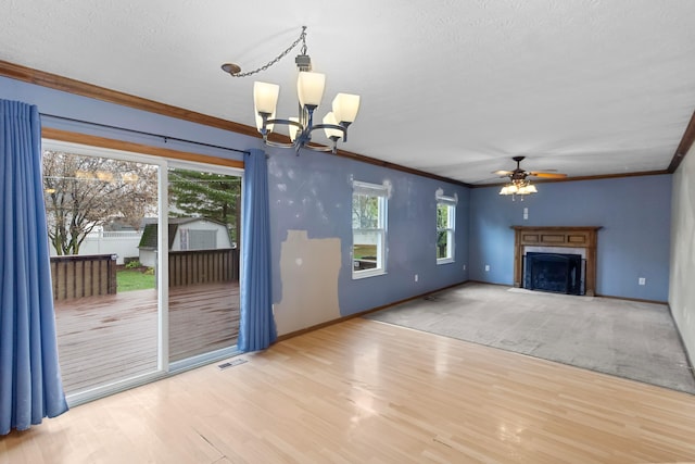 unfurnished living room featuring ceiling fan with notable chandelier, a textured ceiling, light wood-type flooring, and crown molding