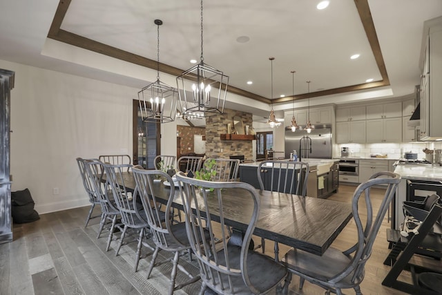 dining room featuring a raised ceiling, a fireplace, dark wood-type flooring, and an inviting chandelier