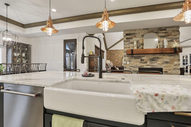 kitchen with light stone counters, stainless steel dishwasher, sink, decorative light fixtures, and a stone fireplace