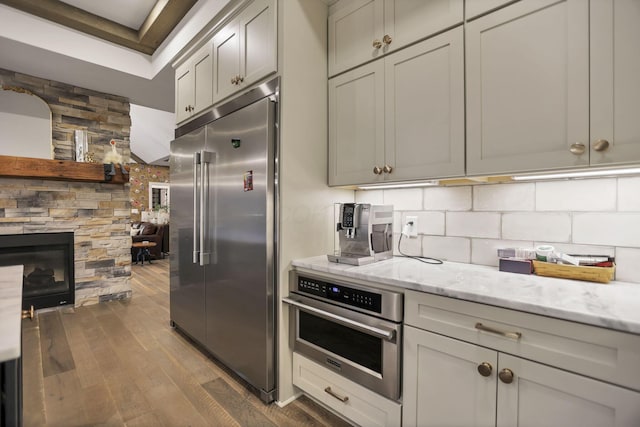 kitchen with gray cabinetry, a stone fireplace, dark hardwood / wood-style floors, light stone countertops, and stainless steel appliances