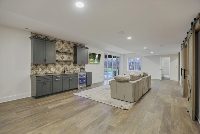 living room featuring a barn door, light hardwood / wood-style floors, sink, and wine cooler