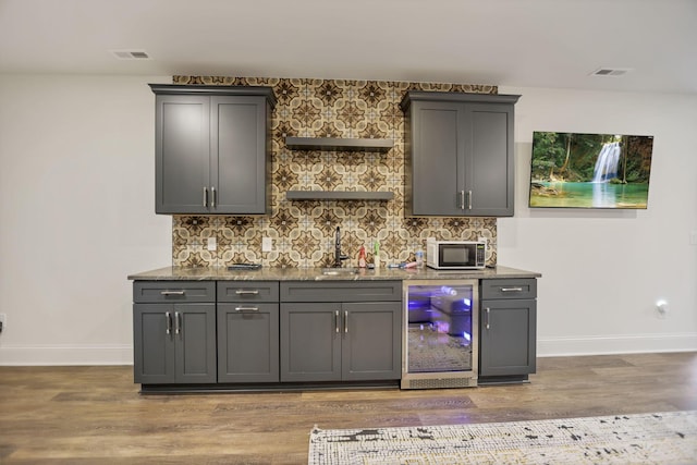 bar featuring decorative backsplash, wood-type flooring, gray cabinets, and sink