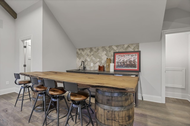 bar with sink, dark wood-type flooring, tasteful backsplash, wooden counters, and lofted ceiling