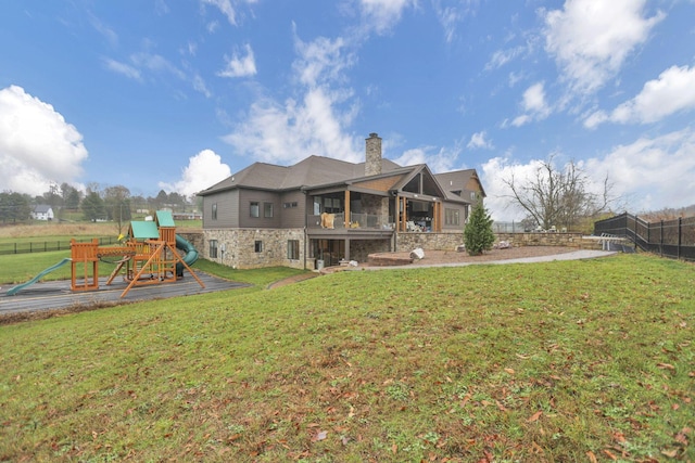 back of house featuring a lawn, a balcony, and a playground