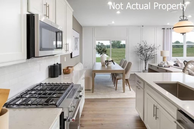 kitchen featuring appliances with stainless steel finishes, light wood-type flooring, sink, decorative light fixtures, and white cabinets