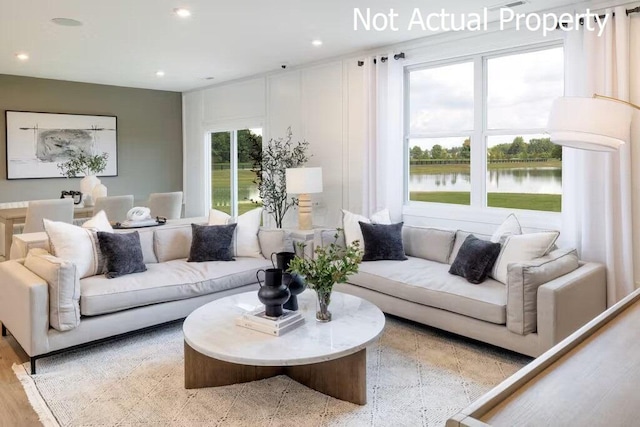 living room with light hardwood / wood-style floors, a water view, and a wealth of natural light