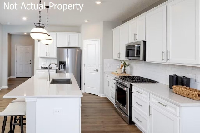 kitchen featuring sink, hanging light fixtures, stainless steel appliances, an island with sink, and white cabinets