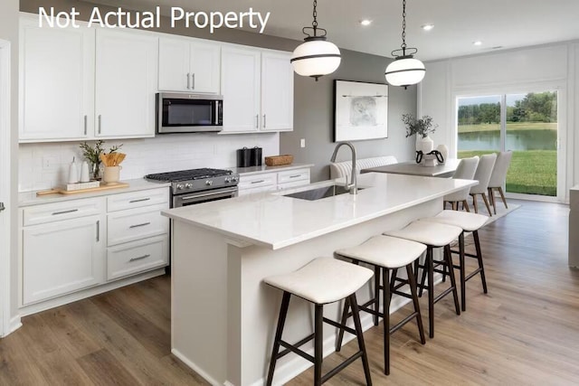 kitchen featuring appliances with stainless steel finishes, a breakfast bar, sink, white cabinets, and an island with sink