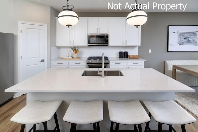 kitchen featuring appliances with stainless steel finishes, tasteful backsplash, hanging light fixtures, and a center island with sink