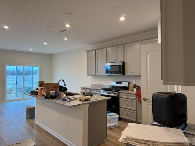 kitchen with sink, stainless steel appliances, light stone counters, light hardwood / wood-style flooring, and a kitchen island with sink