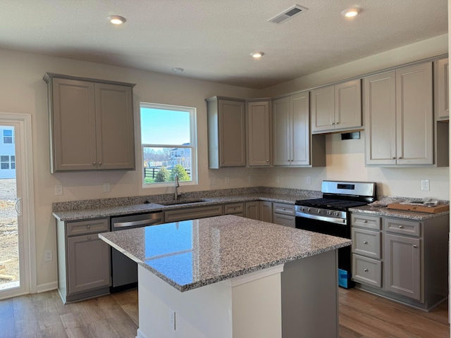 kitchen with light stone countertops, stainless steel appliances, sink, light hardwood / wood-style floors, and a kitchen island