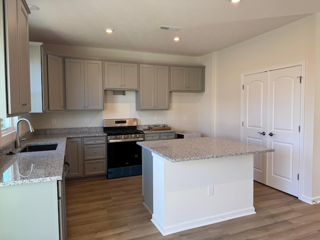 kitchen featuring stainless steel range, a center island, sink, light stone counters, and hardwood / wood-style floors