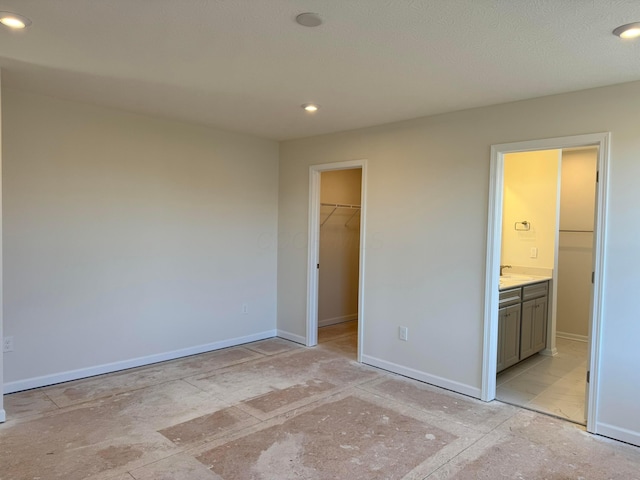 unfurnished bedroom with a closet, a spacious closet, a textured ceiling, and ensuite bath