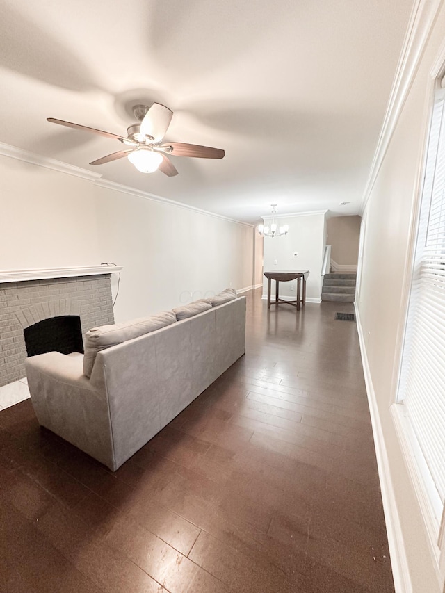 unfurnished living room with ceiling fan with notable chandelier, dark wood-type flooring, crown molding, and a brick fireplace