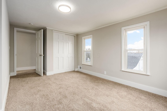 unfurnished bedroom featuring multiple windows, crown molding, a closet, and carpet