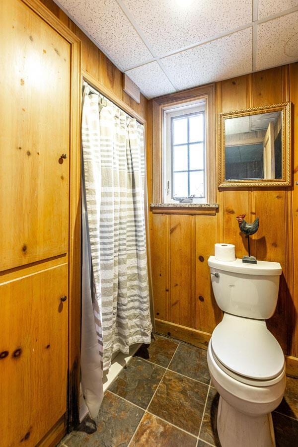 bathroom with a paneled ceiling, toilet, and wooden walls