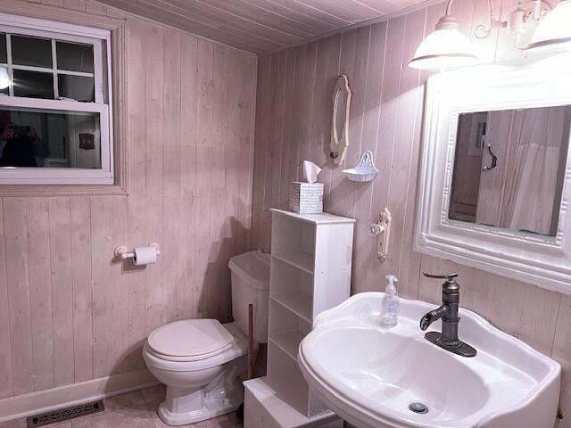 bathroom with sink, wooden ceiling, tile patterned floors, toilet, and wooden walls