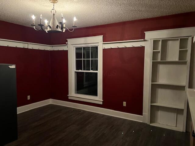 unfurnished room featuring dark hardwood / wood-style flooring, a textured ceiling, and a notable chandelier