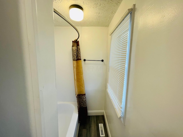 bathroom featuring hardwood / wood-style floors, a textured ceiling, and a tub to relax in