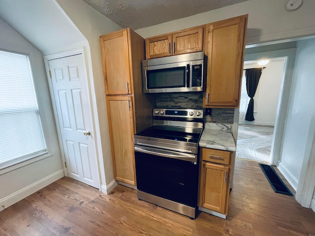 kitchen with tasteful backsplash, light stone countertops, light wood-type flooring, and appliances with stainless steel finishes