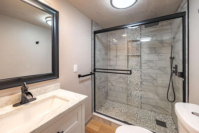 bathroom with vanity, a textured ceiling, a shower with door, hardwood / wood-style floors, and toilet