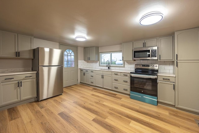 kitchen with decorative backsplash, light wood-type flooring, stainless steel appliances, sink, and gray cabinets