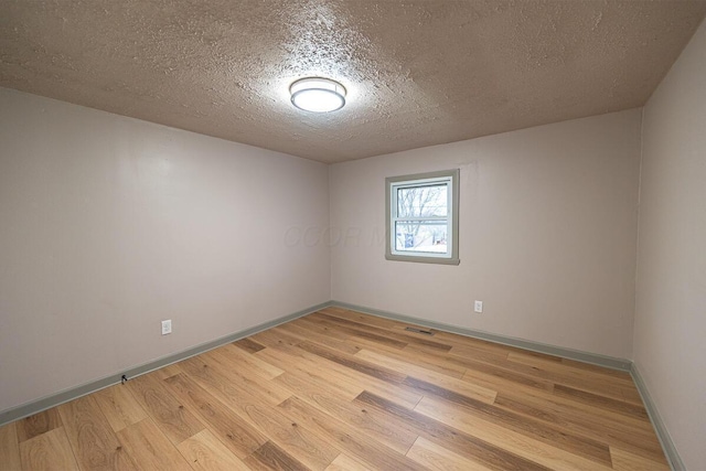 empty room with a textured ceiling and light hardwood / wood-style flooring