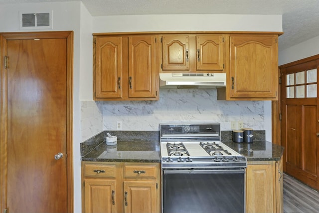 kitchen featuring dark stone countertops, decorative backsplash, black gas stove, and hardwood / wood-style floors