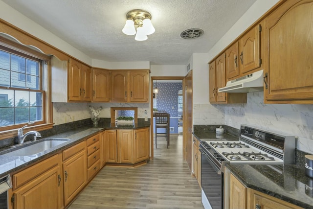 kitchen with backsplash, gas range oven, a textured ceiling, sink, and light hardwood / wood-style flooring