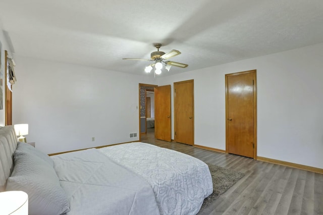 bedroom with ceiling fan, light hardwood / wood-style floors, and two closets