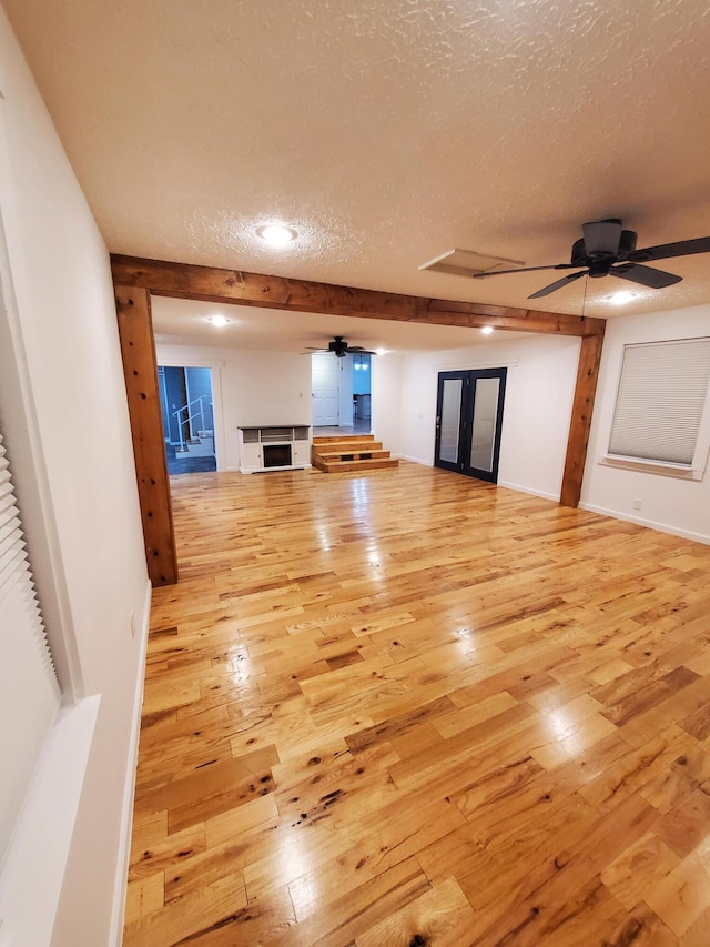 unfurnished living room featuring french doors, a textured ceiling, light wood-type flooring, and ceiling fan