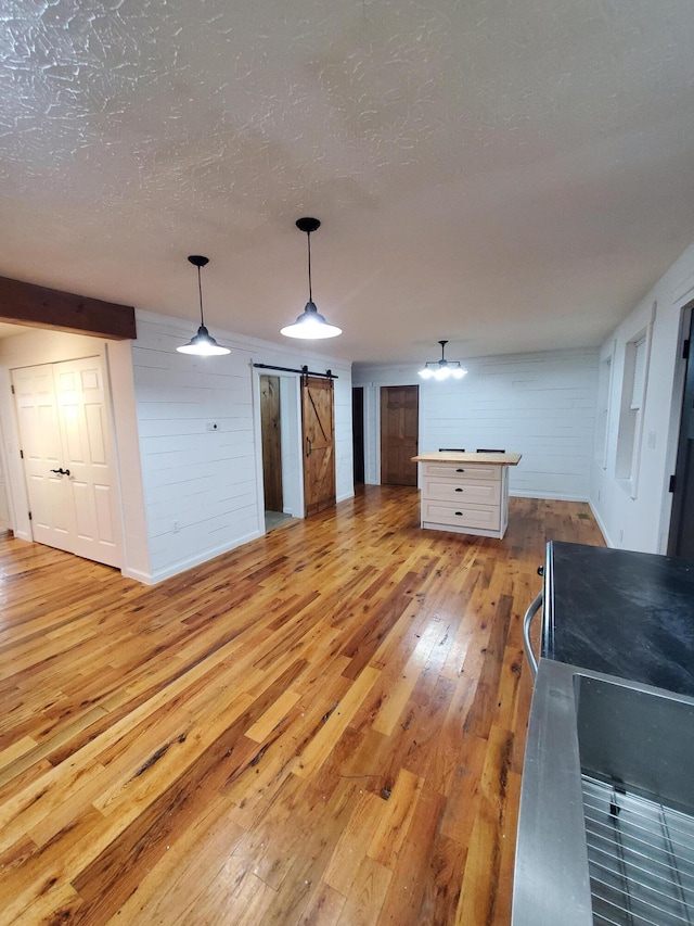 unfurnished living room featuring a textured ceiling, a barn door, light hardwood / wood-style flooring, and wood walls