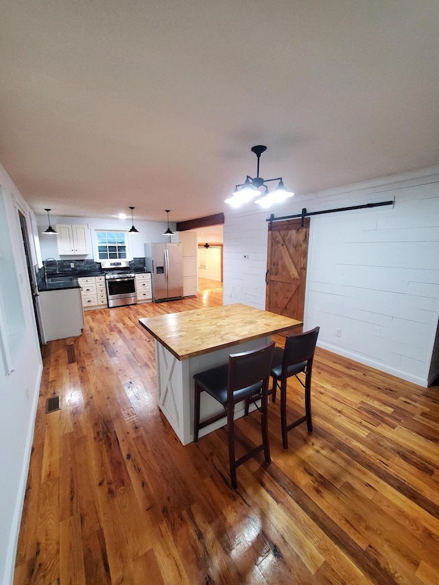 kitchen with white cabinets, hardwood / wood-style flooring, a barn door, decorative light fixtures, and stainless steel appliances