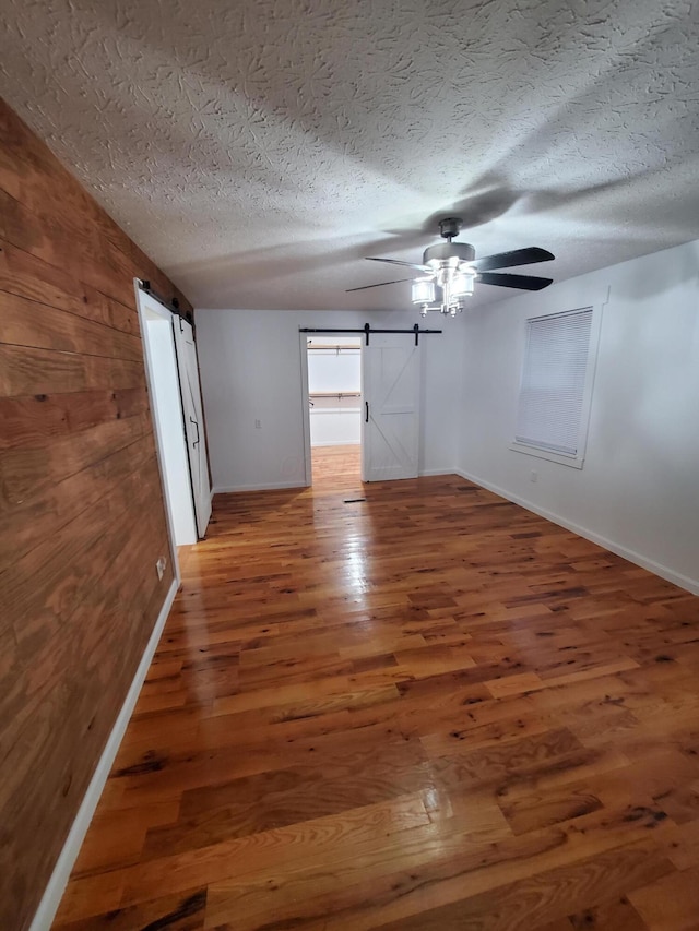 spare room with dark hardwood / wood-style flooring, a barn door, a textured ceiling, and ceiling fan