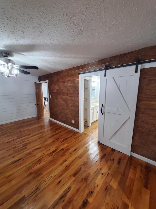 empty room with a textured ceiling, a barn door, hardwood / wood-style flooring, and wood walls