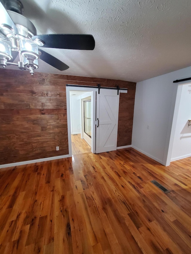 interior space with a textured ceiling, a barn door, hardwood / wood-style flooring, and wooden walls