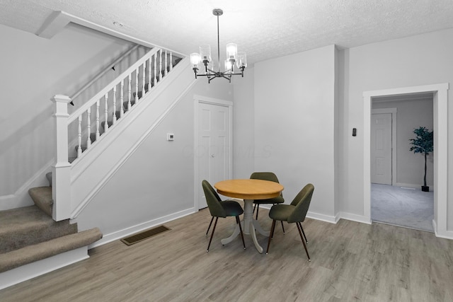 dining room featuring a textured ceiling, an inviting chandelier, and light hardwood / wood-style flooring