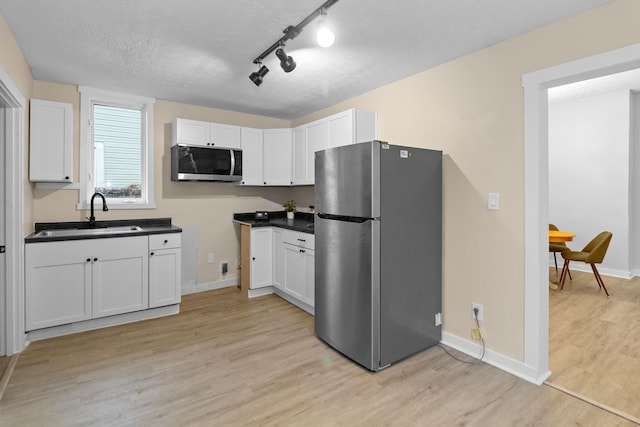 kitchen with sink, a textured ceiling, light hardwood / wood-style floors, white cabinetry, and stainless steel appliances