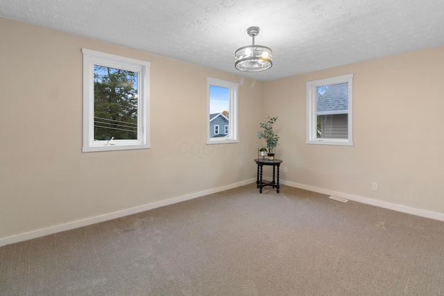 carpeted spare room with a textured ceiling and a notable chandelier