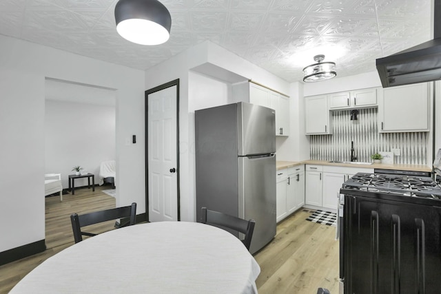 kitchen with sink, gas range, stainless steel fridge, decorative backsplash, and white cabinets